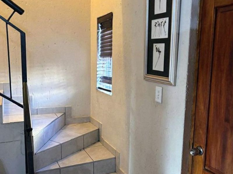 A functional hallway featuring a tiled staircase with a metal handrail and a wooden door, providing access between levels.
