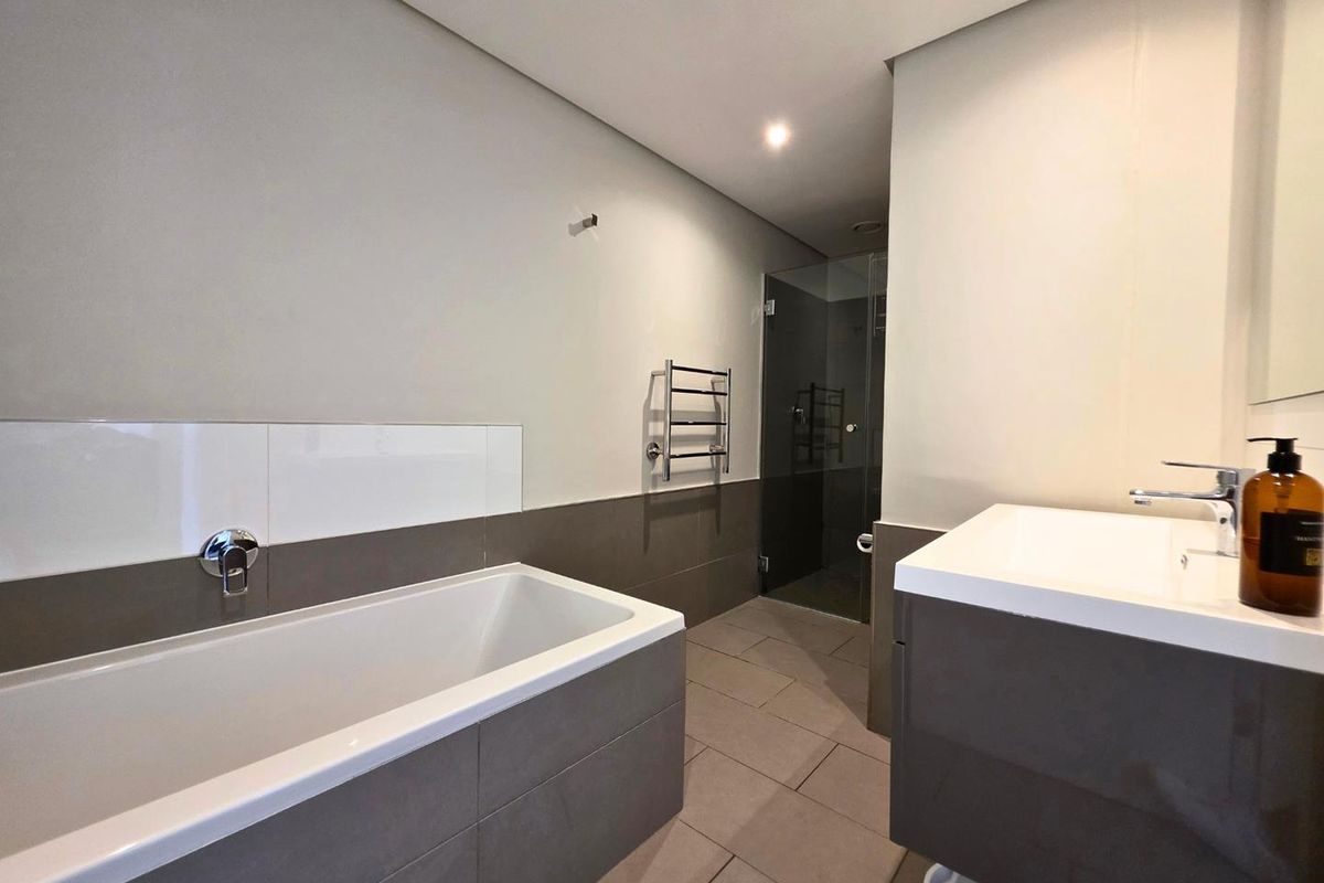 Modern bathroom featuring a built-in bathtub, wall-mounted vanity with basin, heated towel rail, and a separate glass-enclosed shower area.