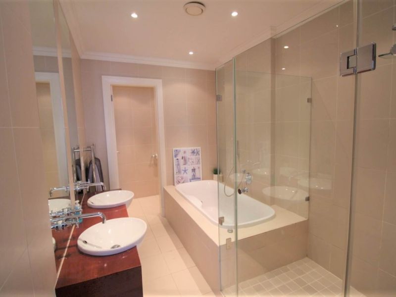 Modern bathroom featuring a double vanity, a built-in bathtub, and a separate glass-enclosed shower with neutral tiling throughout.