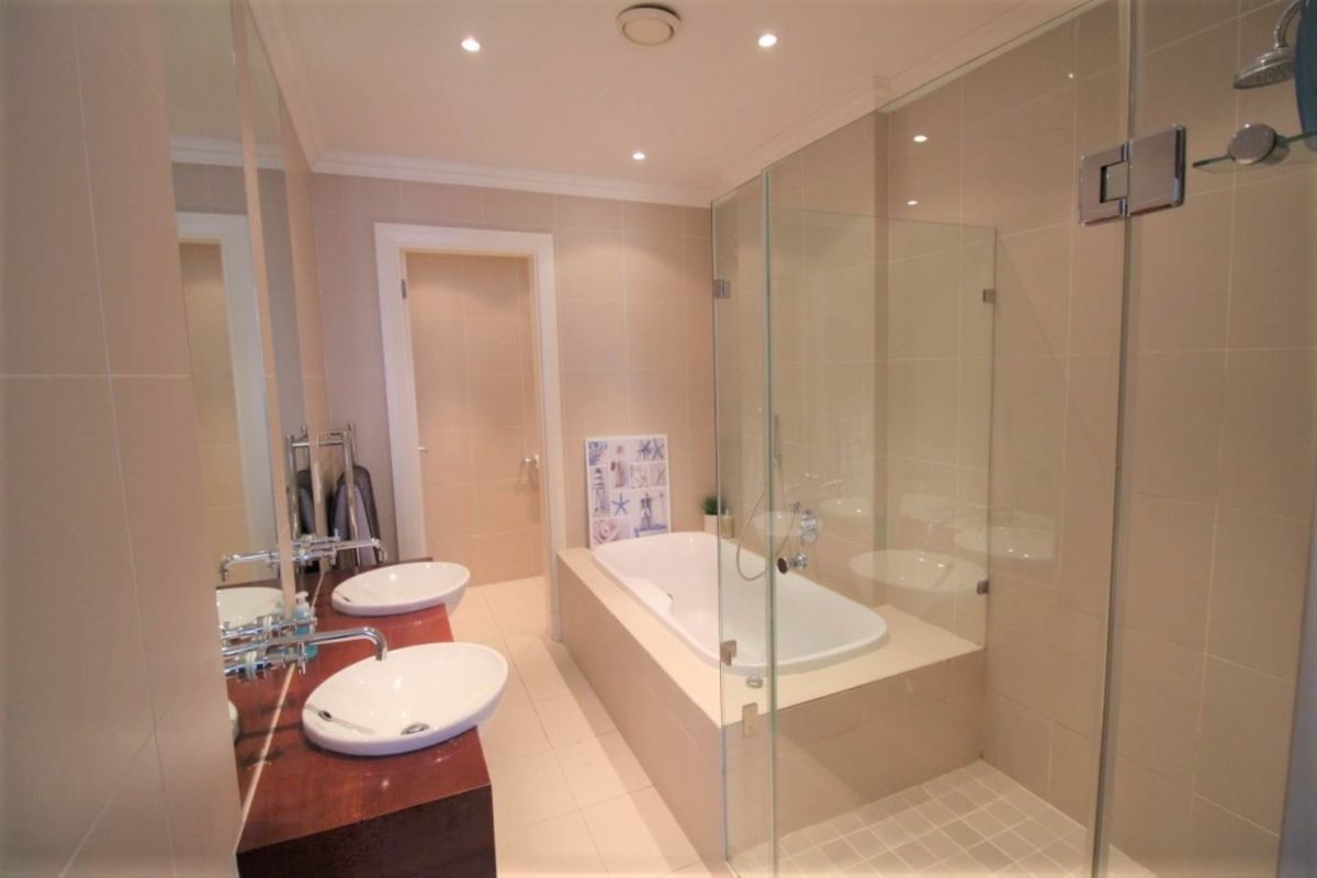 Modern bathroom featuring a double vanity, a built-in bathtub, and a separate glass-enclosed shower with neutral tiling throughout.