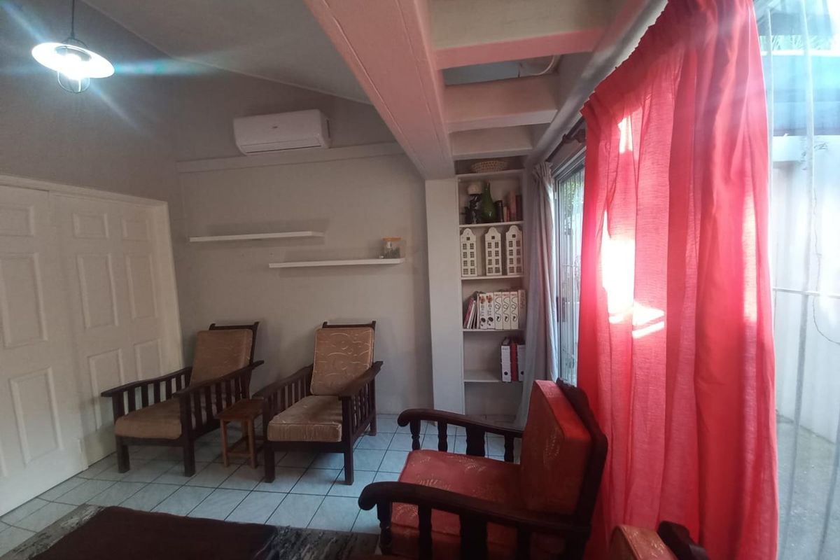 A living room featuring tiled flooring, exposed ceiling beams, built-in shelving, and a split-system air conditioner with access to an outdoor area.
