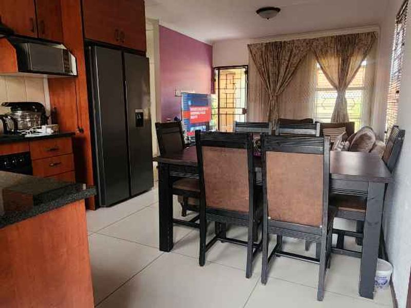 Open-plan kitchen and dining area featuring wooden cabinetry, granite countertops, and large format floor tiles.
