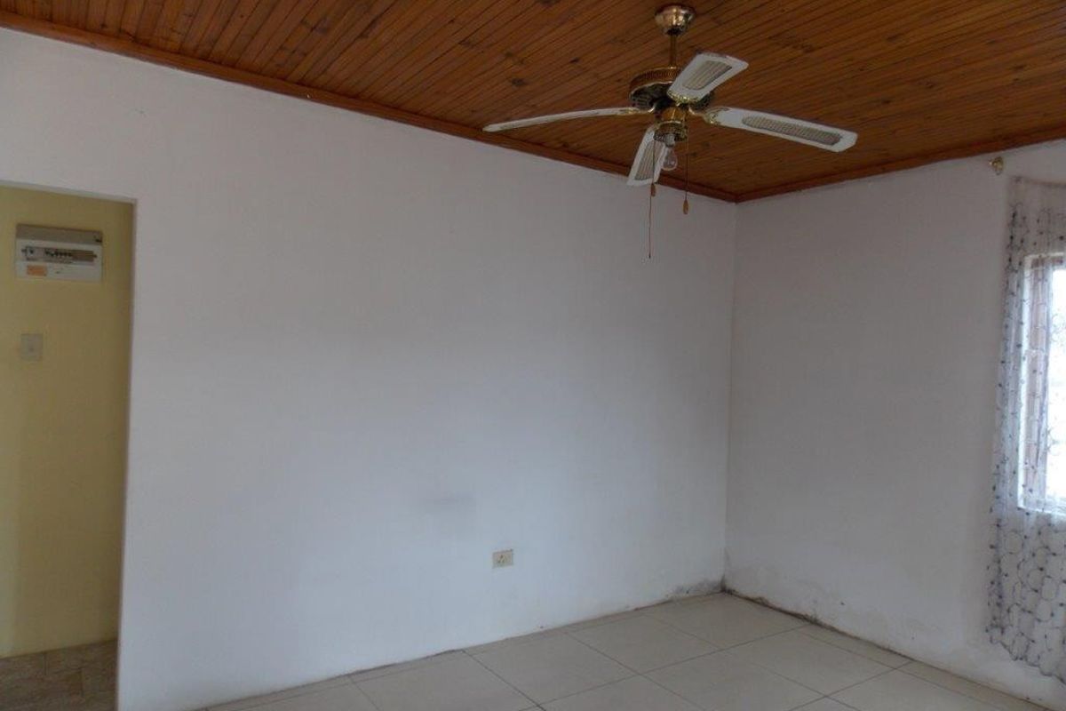 An empty living room featuring a timber tongue and groove ceiling, ceiling fan, and tiled flooring, requiring minor cosmetic attention to walls and skirting.