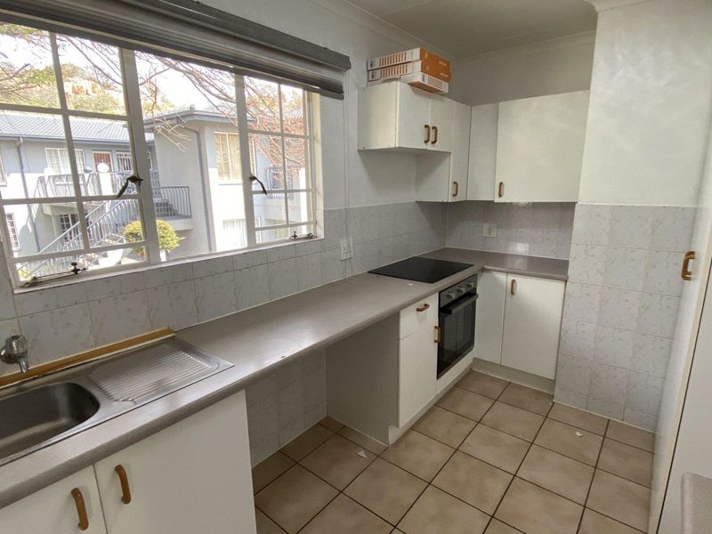 A functional kitchen featuring white built-in cabinetry, laminate countertops, a stainless steel sink, and an integrated electric oven and hob with tiled splashbacks.
