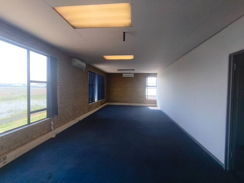 Spacious, empty office area featuring exposed brick walls, large windows with natural light, carpeted flooring, and dual split-system air conditioning units.