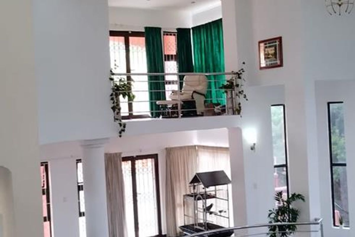 Spacious double-volume living area featuring a mezzanine level, elegant curved staircase with stainless steel balustrades, and polished dark floor tiles.