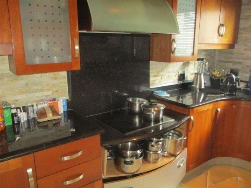A functional kitchen featuring wooden cabinetry, dark granite countertops, a built-in electric hob with an extractor fan, and a textured stone tile backsplash.