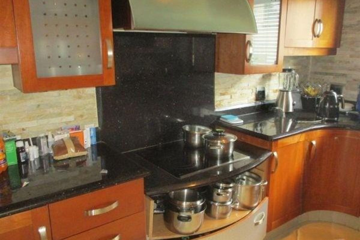 A functional kitchen featuring wooden cabinetry, dark granite countertops, a built-in electric hob with an extractor fan, and a textured stone tile backsplash.