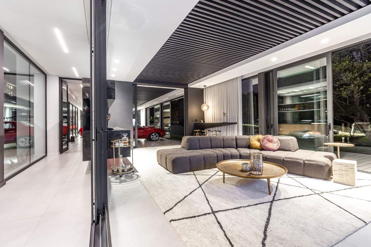 Modern open-plan living area featuring a striking slatted ceiling, large format floor tiles, and expansive floor-to-ceiling glass doors opening to the exterior.