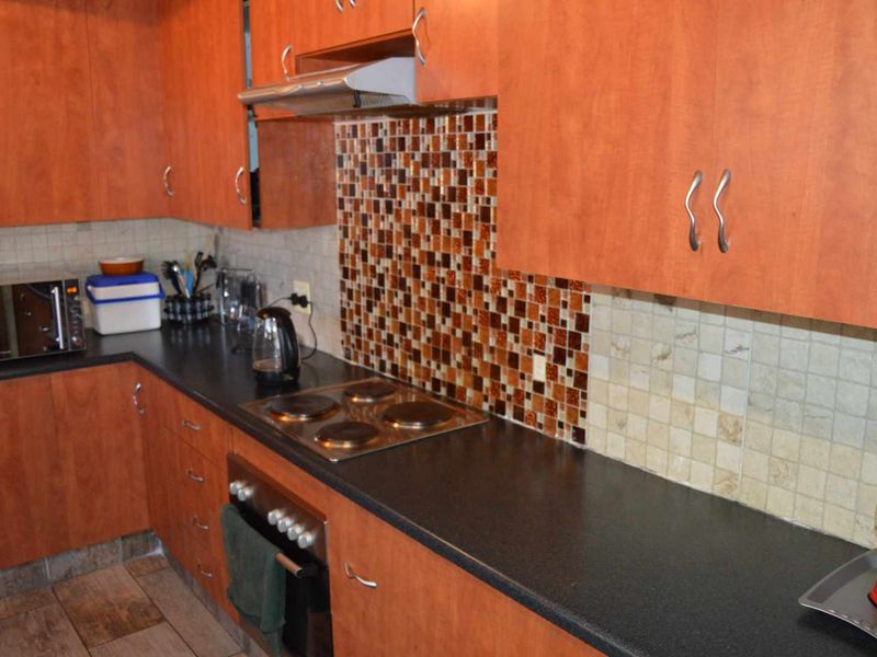 A functional kitchen featuring wood-look cabinetry, dark laminate countertops, a built-in electric oven and hob, and a decorative mosaic tile backsplash.