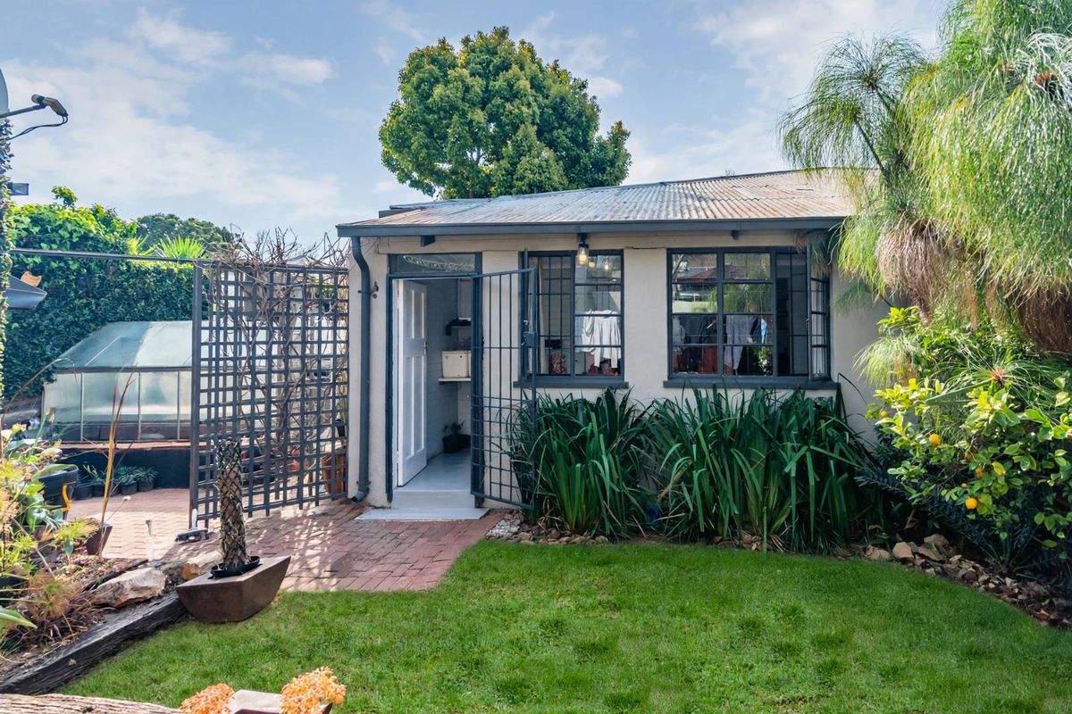 Rear view of a detached outbuilding featuring a corrugated metal roof, steel-framed windows, and a security gate, set within a landscaped garden.