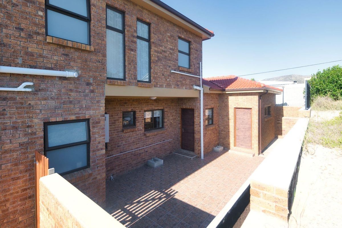 A view of the rear exterior of the house, featuring a paved patio area, brick facade, and tiled roof.