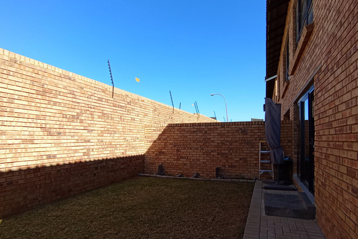 A private rear courtyard featuring face-brick walls, perimeter electric fencing, and a paved walkway leading to the apartment entrance.