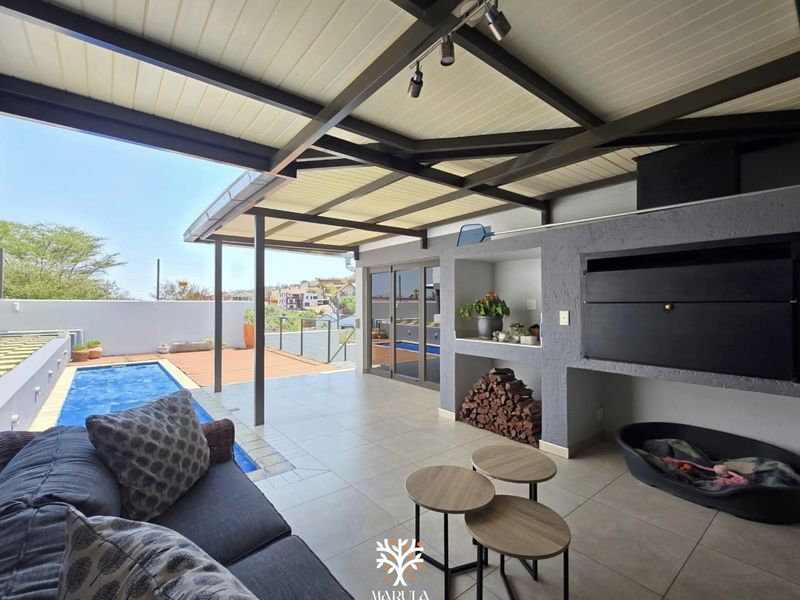Covered outdoor patio featuring a built-in braai, tiled flooring, and direct access to a swimming pool, ideal for alfresco entertaining.