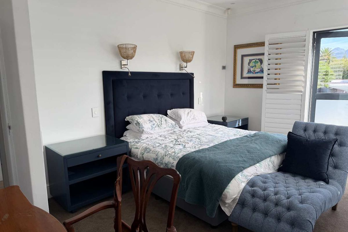 A well-maintained bedroom featuring built-in wall sconces, plantation shutters, and neutral carpeting, offering a comfortable and bright living space.