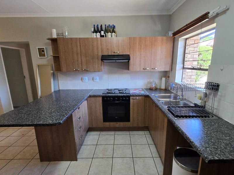 Functional kitchen featuring wood-look cabinetry, granite-style countertops, built-in oven with hob, and tiled flooring with a bright window for natural light.