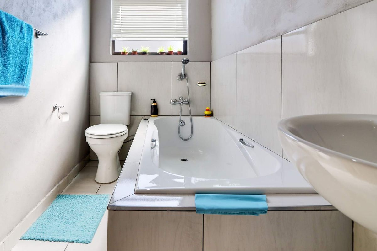 A functional bathroom featuring a built-in bathtub, toilet, and pedestal basin with neutral wall tiling and natural light from a window.