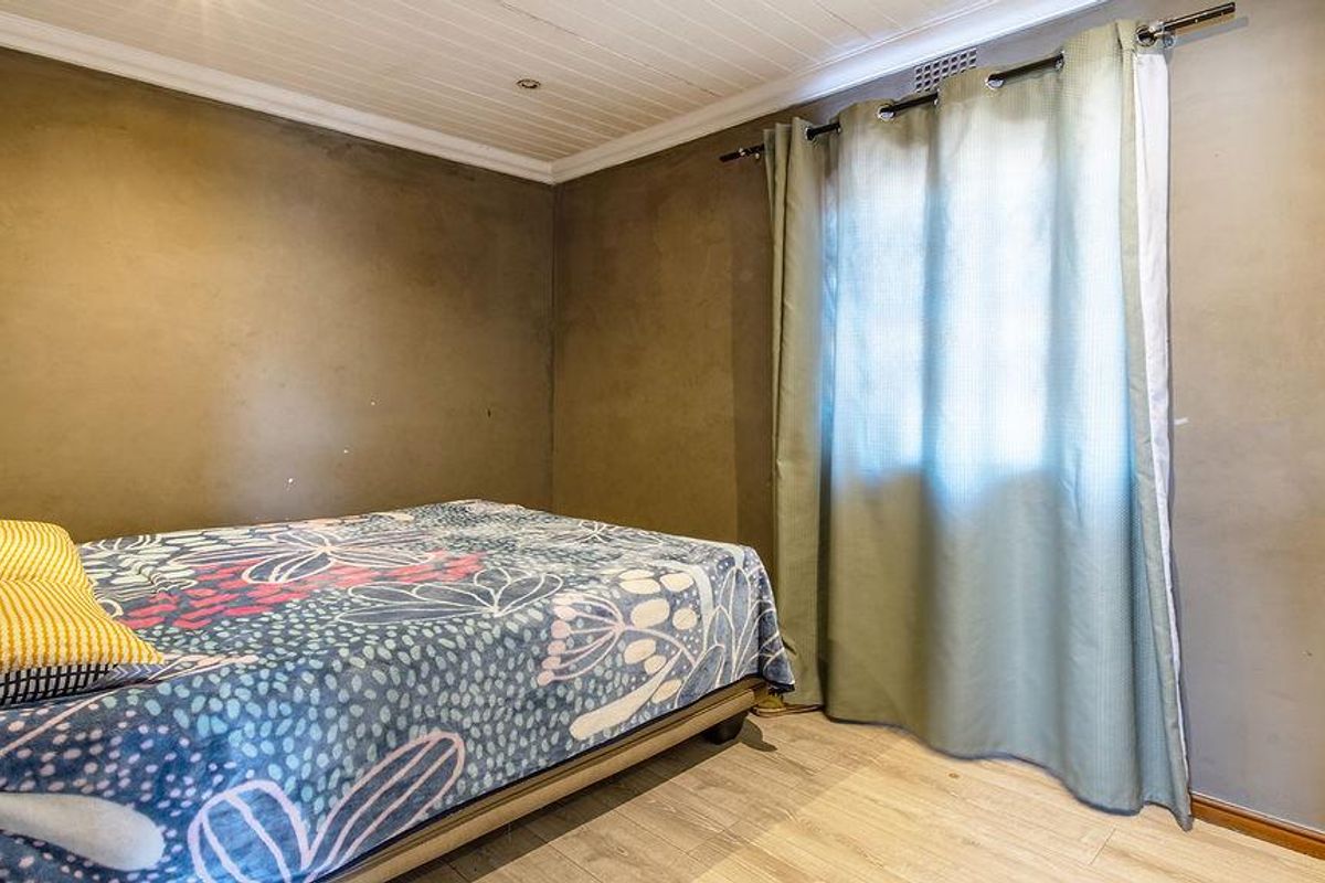 A bedroom featuring timber-look laminate flooring, a tongue-and-groove ceiling, and a built-in wardrobe, requiring cosmetic updates to the wall finishes.