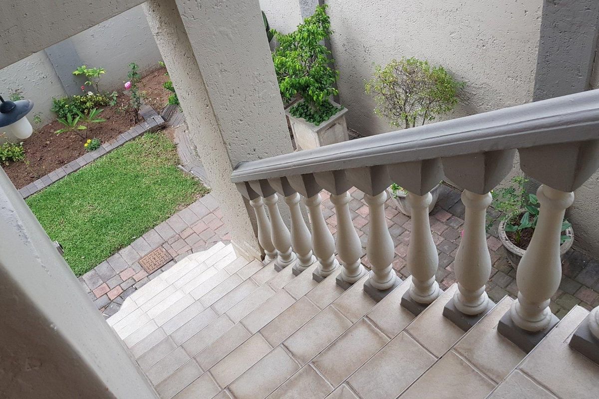 An elevated view of a tiled staircase with a concrete balustrade leading down to a small paved courtyard and garden area.