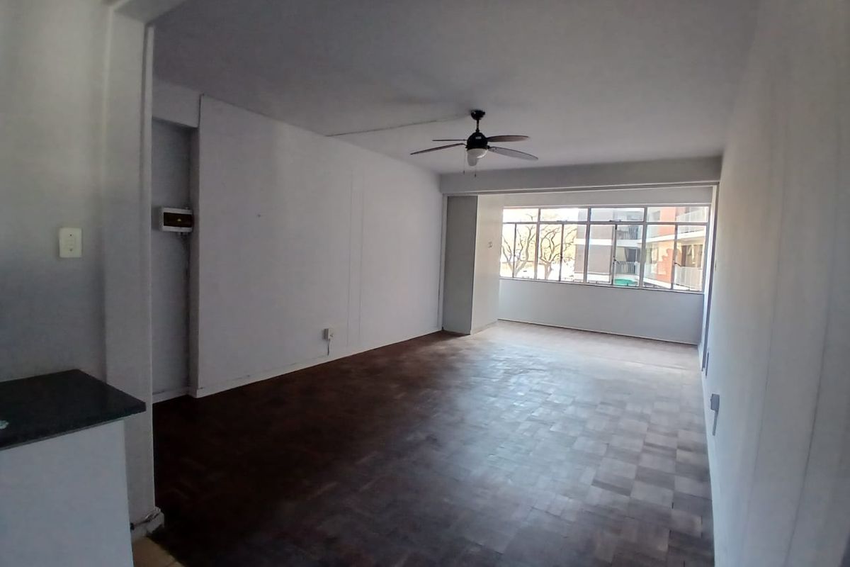 Spacious, empty living area featuring classic parquet flooring, a ceiling fan, and large windows providing natural light.