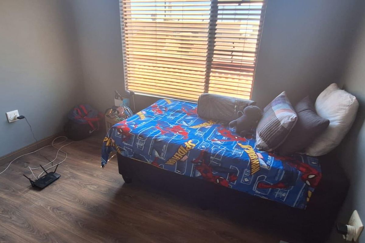 A bedroom featuring wood-look laminate flooring and horizontal window blinds, providing a functional and neutral space.