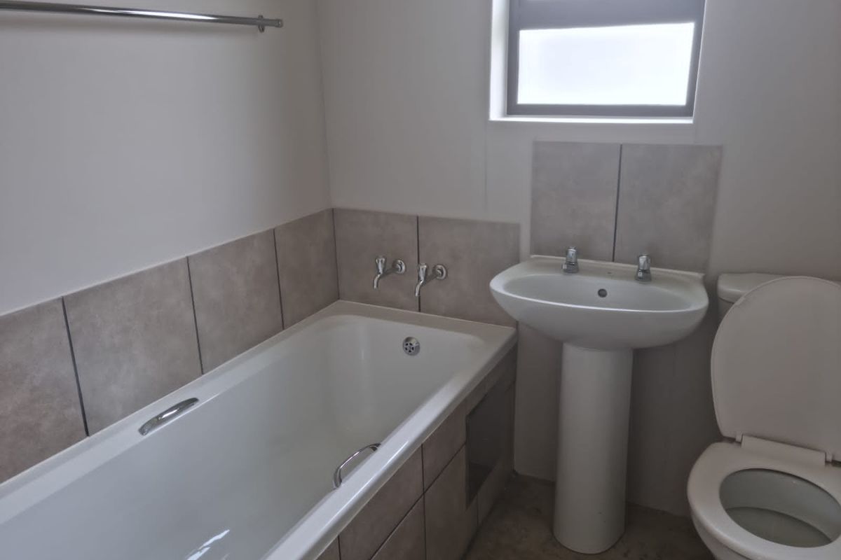 A functional bathroom featuring a built-in bathtub with tiled surround, a pedestal basin, and a standard toilet.