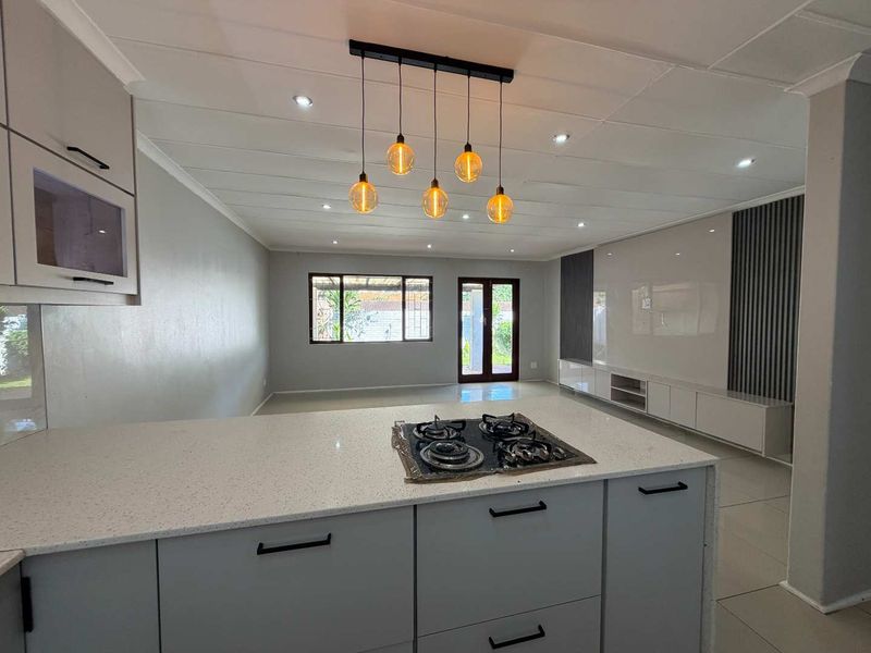 Modern open-plan living area featuring a sleek kitchen island with gas hob, contemporary cabinetry, and a built-in media wall with neutral finishes.