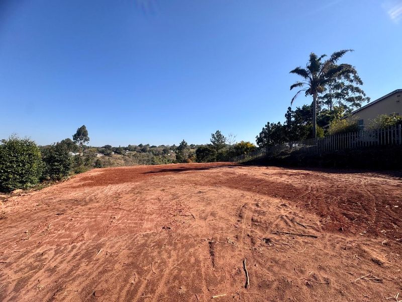 A cleared residential plot of land featuring a level building site with perimeter fencing and surrounding greenery.