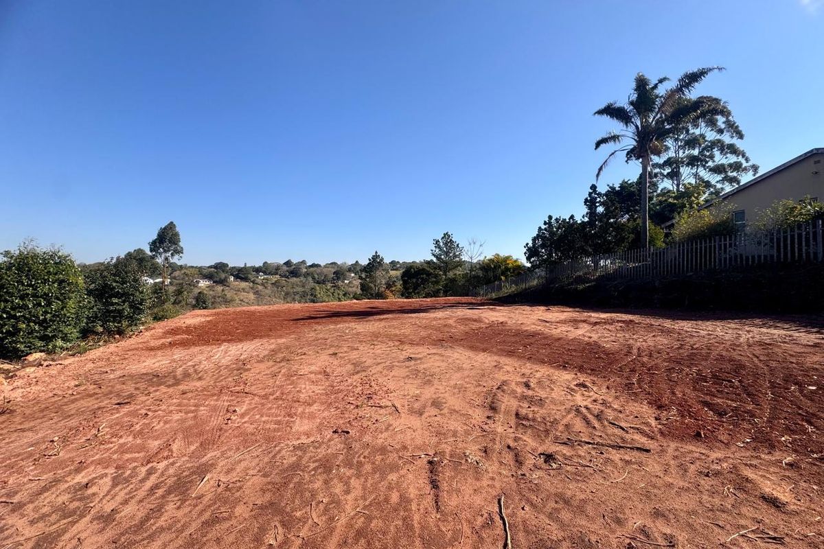 A cleared residential plot of land featuring a level building site with perimeter fencing and surrounding greenery.