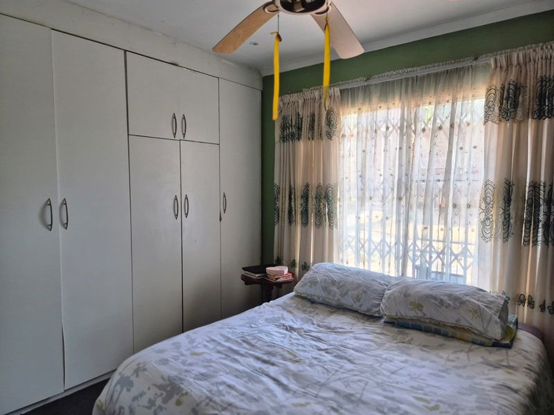 A bedroom featuring floor-to-ceiling built-in cupboards, a ceiling fan, and a window fitted with a security gate.