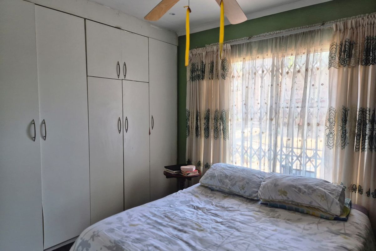 A bedroom featuring floor-to-ceiling built-in cupboards, a ceiling fan, and a window fitted with a security gate.