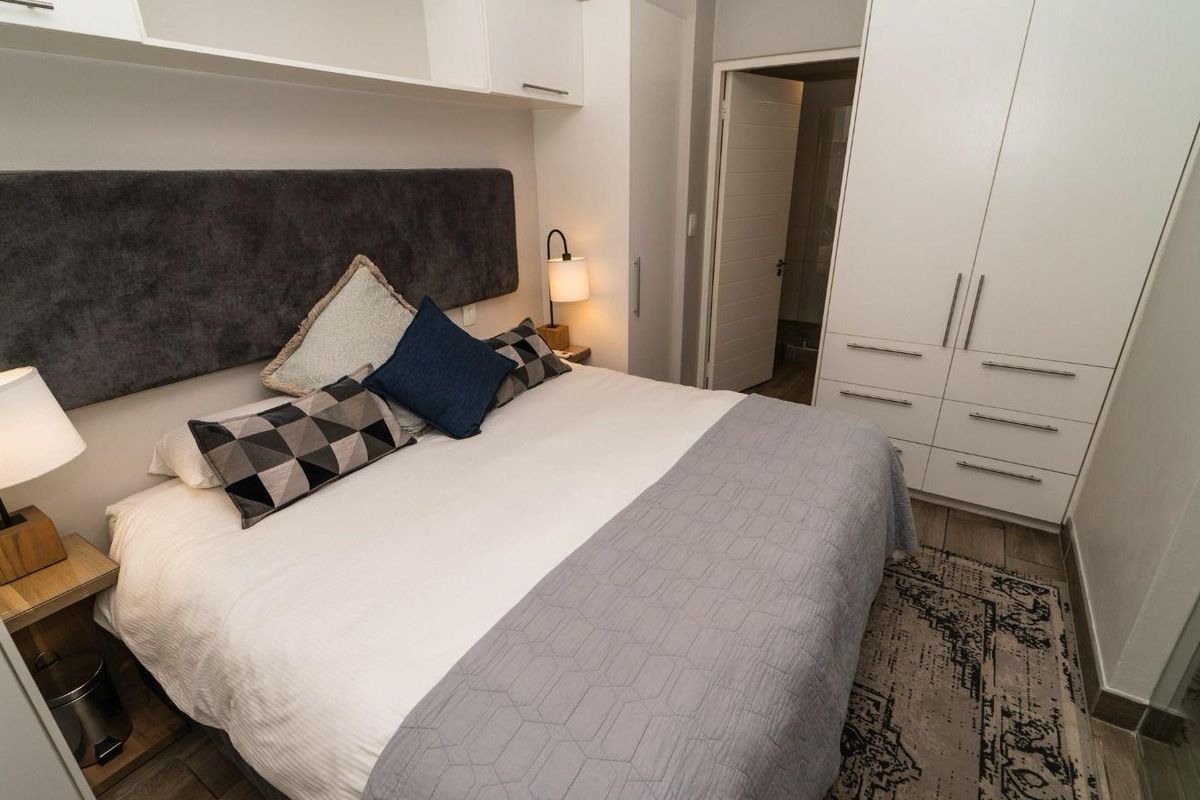 A well-maintained bedroom featuring built-in wardrobes, overhead storage cabinetry, and tiled flooring, providing a clean and functional living space.