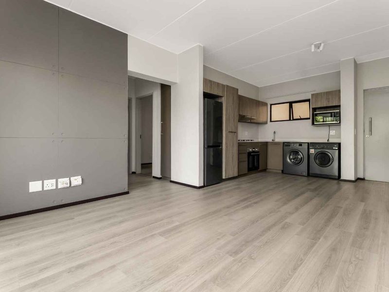 Modern open-plan living area featuring light laminate flooring, a sleek feature wall, and a compact kitchen with built-in appliances and cabinetry.