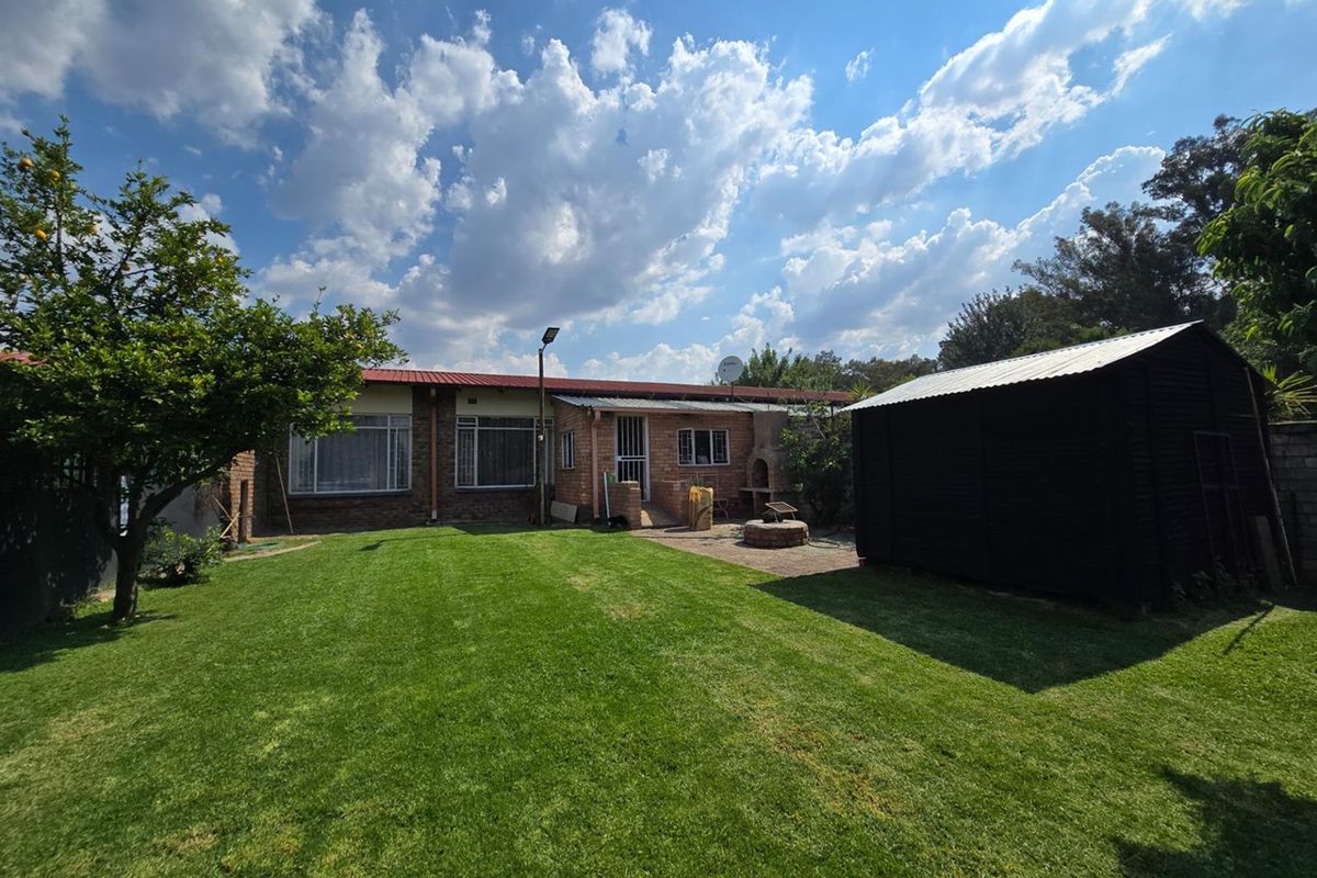 Spacious rear garden featuring a well-maintained lawn, paved patio area with a built-in braai, and a detached storage shed.