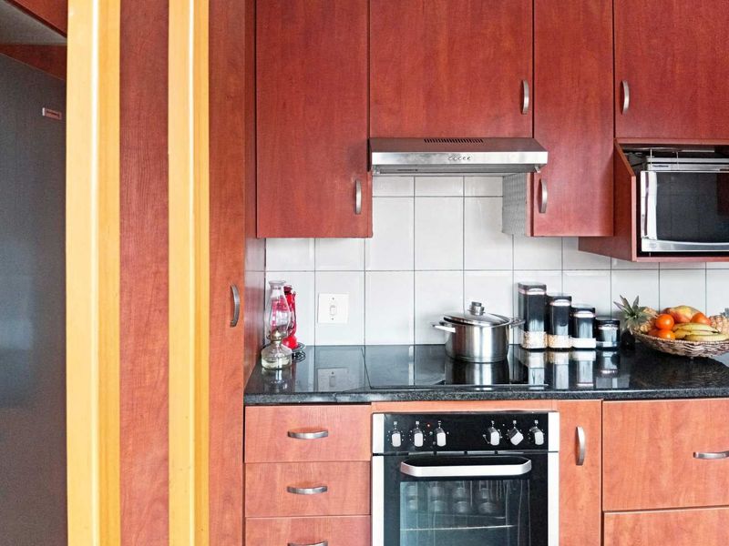 A functional kitchen featuring warm-toned wooden cabinetry, granite countertops, a tiled backsplash, and integrated appliances including an oven, hob, and microwave.