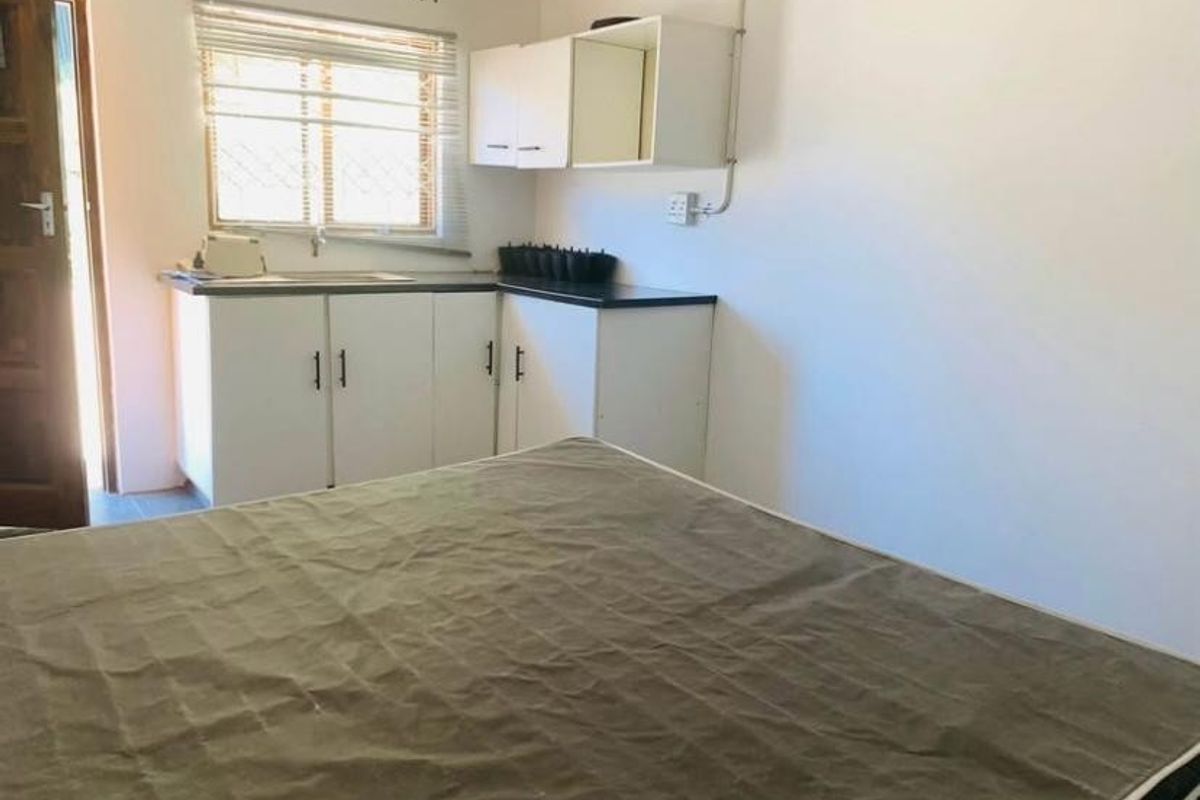 A small kitchen area featuring basic white cabinetry, a laminate countertop, and a sink, with exposed electrical conduit visible on the wall.