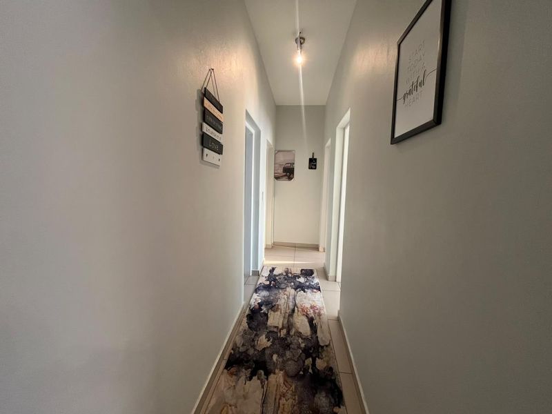 A clean and simple residential hallway featuring neutral wall finishes and tiled flooring, providing access to various rooms within the apartment.