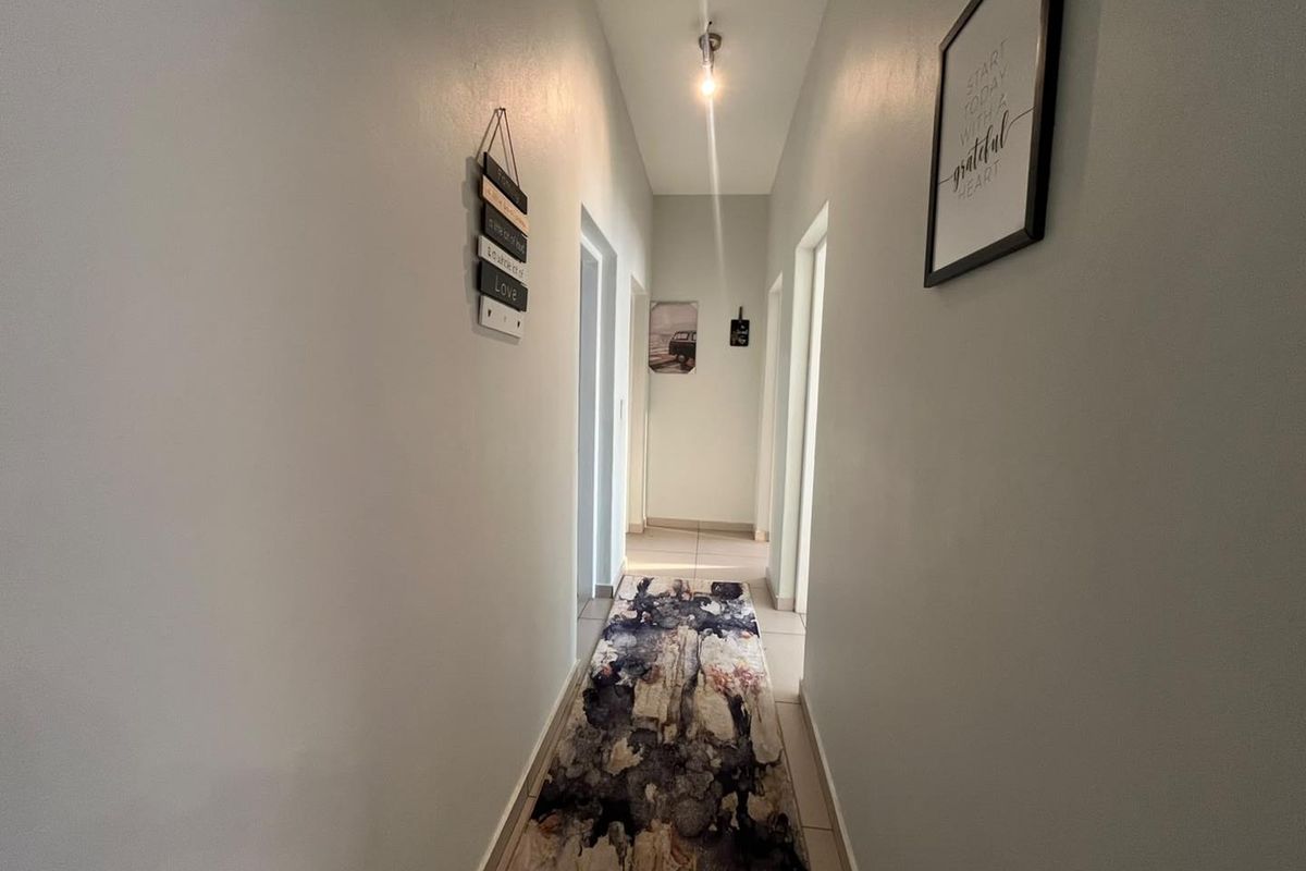 A clean and simple residential hallway featuring neutral wall finishes and tiled flooring, providing access to various rooms within the apartment.