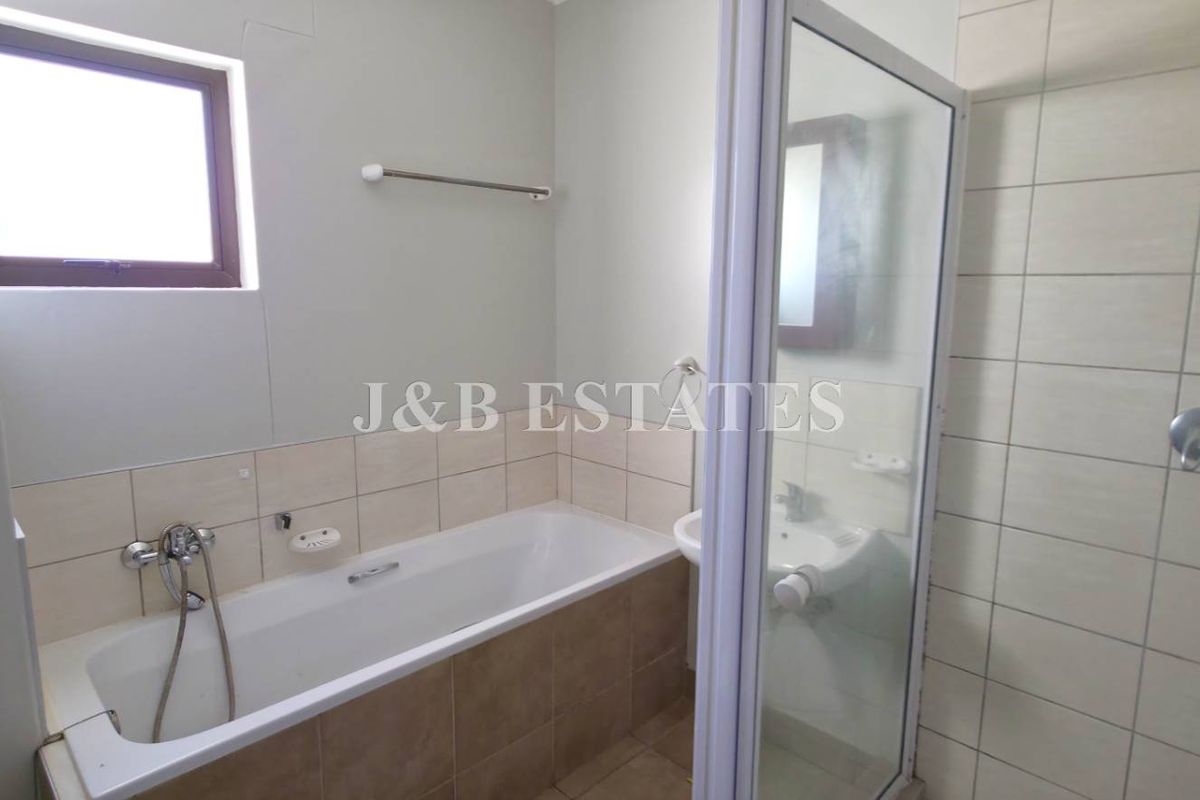 A functional bathroom featuring a built-in bathtub, separate glass-enclosed shower, and wall-mounted basin with neutral tiling.