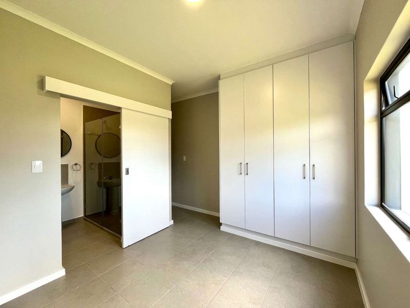 A bright, empty bedroom featuring neutral tiled flooring, ample built-in cupboard space, and a sliding door leading to an en-suite bathroom.