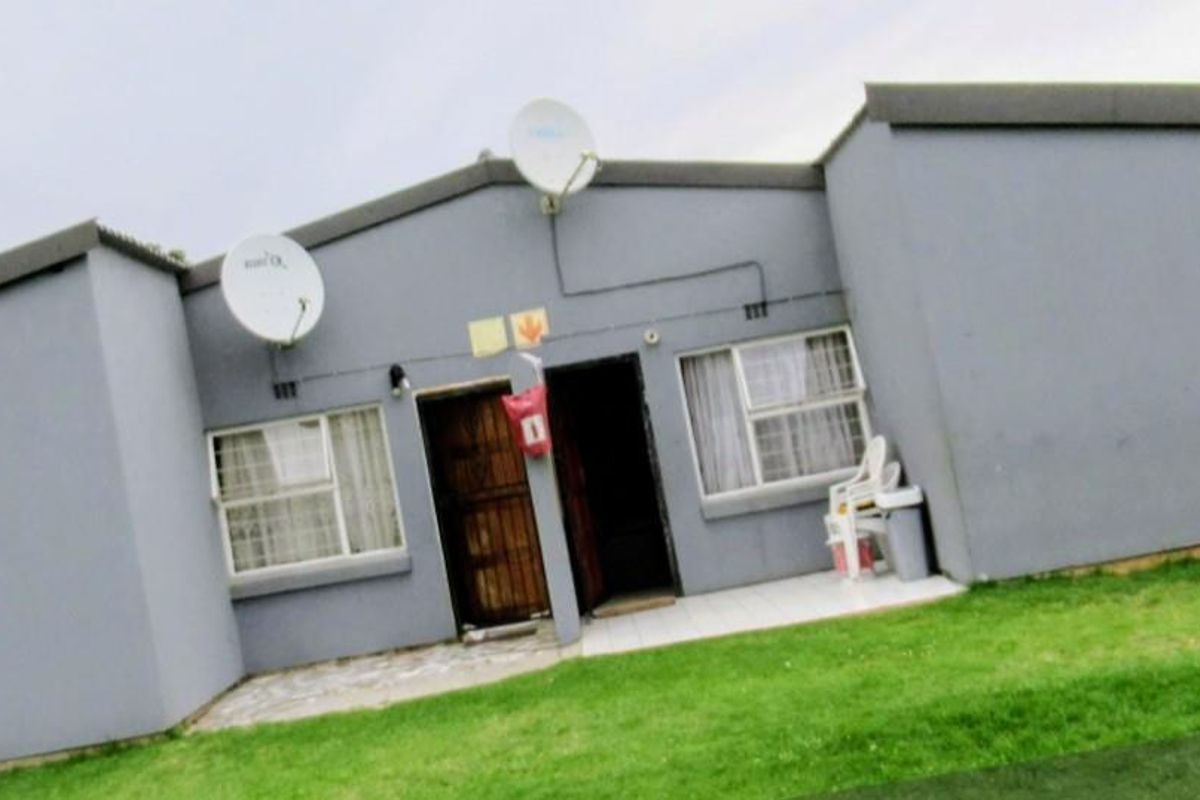 Rear exterior view of the townhouse featuring a tiled patio area, security gate, and satellite dish installation.