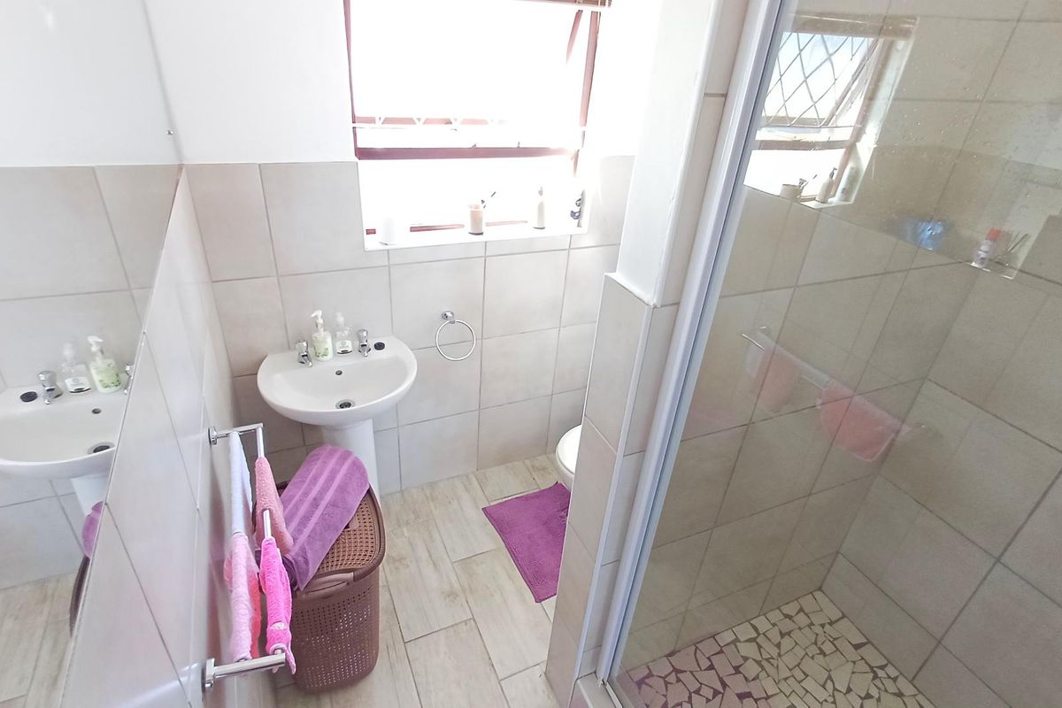 A functional bathroom featuring a pedestal basin, a shower enclosure with tiled walls, and neutral floor tiling.