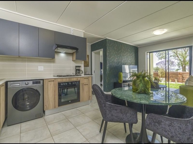 Open-plan kitchen and living area featuring modern cabinetry, integrated appliances, tiled flooring, and direct access to an outdoor patio through sliding glass doors.
