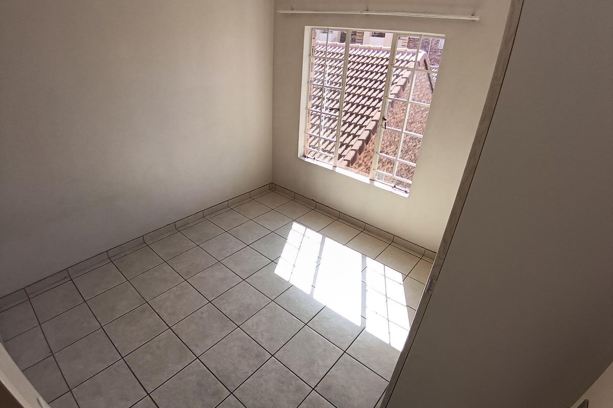 A clean, empty bedroom featuring neutral tiled flooring, a window with security bars, and a curtain rail, ready for personalization.