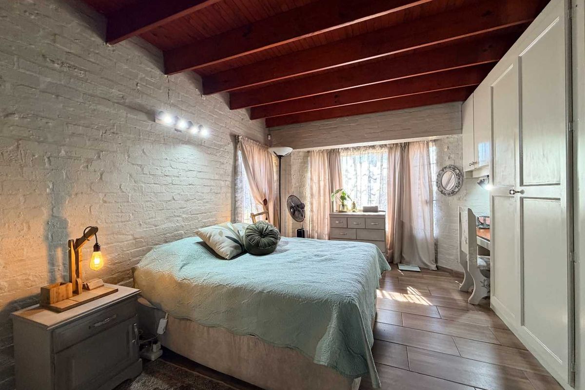 A cozy bedroom featuring exposed timber ceiling beams, painted brick walls, tiled flooring, and a large built-in wardrobe for ample storage.