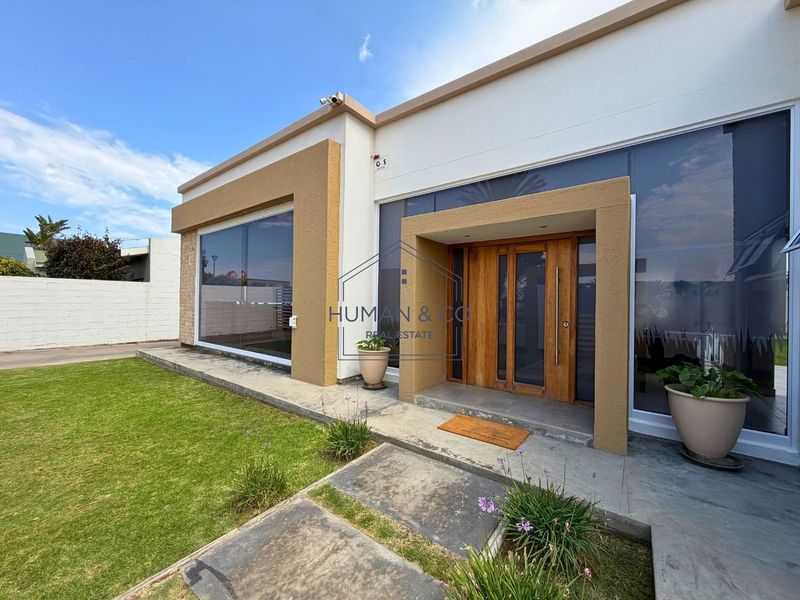 Modern front facade featuring a prominent timber entrance door, large glass windows, and a clean concrete walkway leading to the main entry.