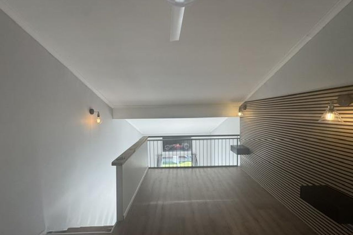 A bright, modern mezzanine living area featuring sloped ceilings, contemporary slatted timber wall paneling, and a sleek metal balustrade overlooking the lower level.