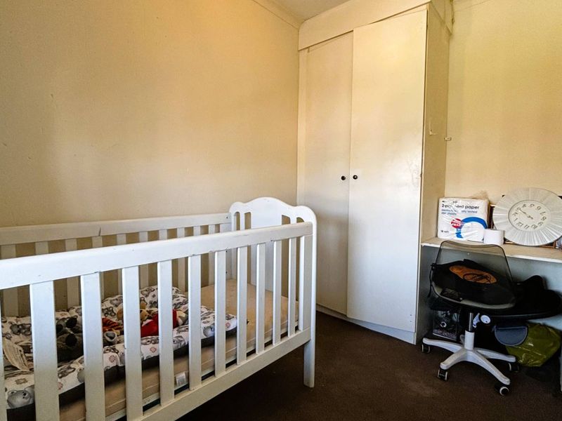 A compact bedroom featuring a built-in wardrobe and a small integrated desk area, finished with neutral wall paint and carpet flooring.