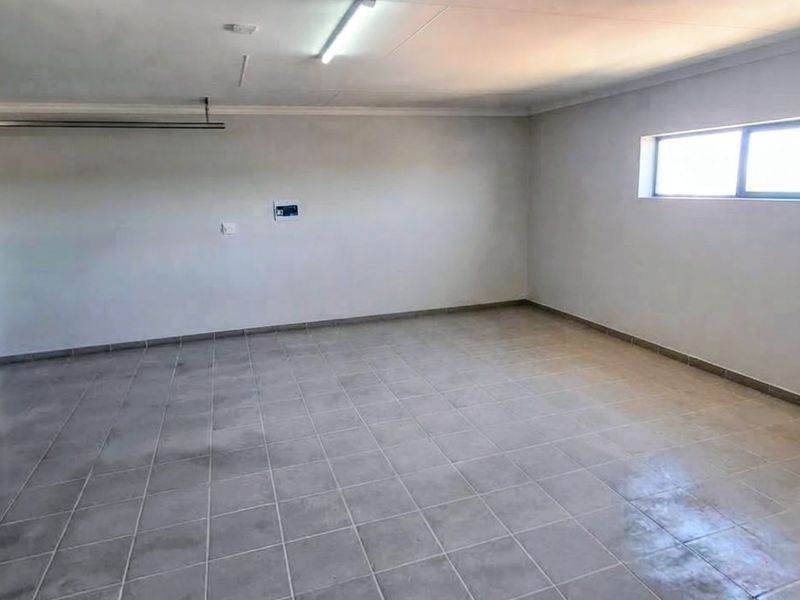 A clean, empty double garage featuring tiled flooring, a sectional garage door, and a window, providing ample space for vehicle storage or a workshop.