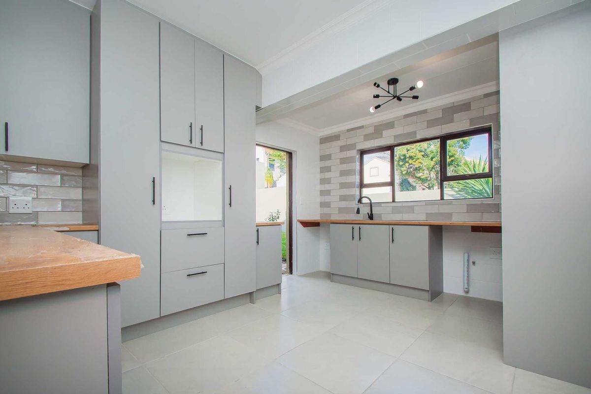 Modern kitchen featuring light grey cabinetry, wooden countertops, subway tile backsplash, and a contemporary black faucet with direct access to the exterior.